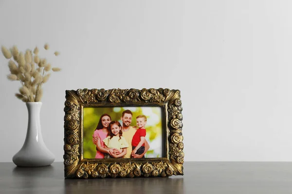 Vintage square frame with family photo and vase of dry flowers on wooden table, space for text