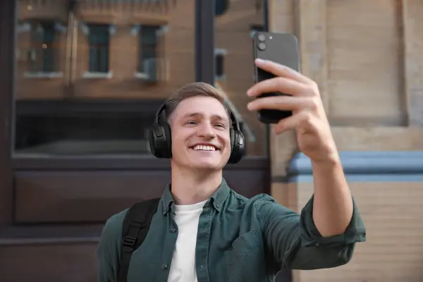 Smiling man in headphones taking selfie outdoors
