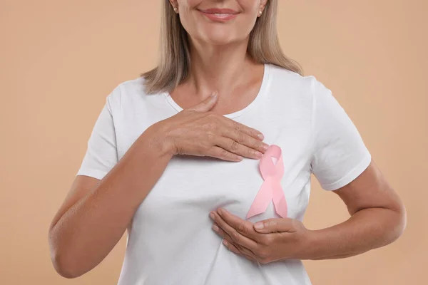 Breast cancer awareness. Woman with pink ribbon doing self-examination on light brown background, closeup