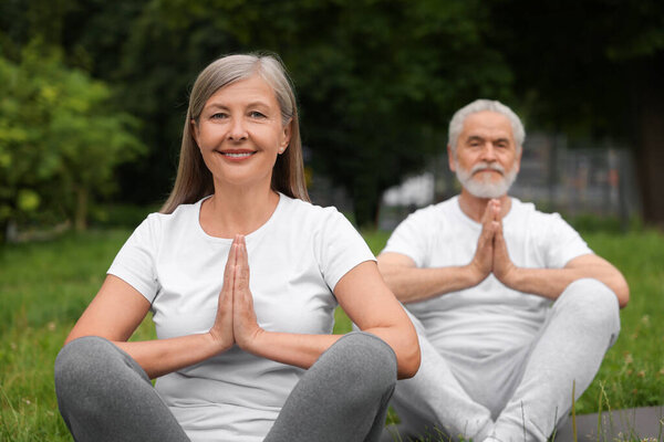 Senior couple practicing yoga in park, selective focus