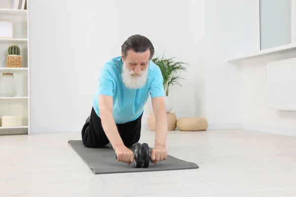 Senior man exercising with abdominal wheel at home. Sports equipment