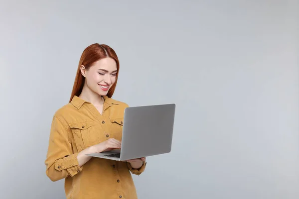 在灰色背景下与笔记本电脑一起工作的年轻女性微笑 文字空间 — 图库照片