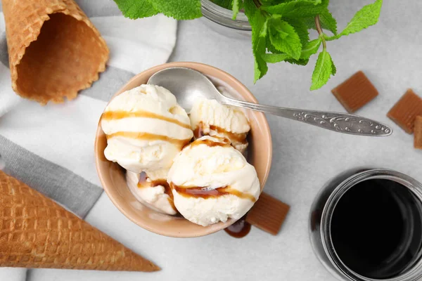 Scoops of ice cream with caramel sauce, wafer cones and candies on light grey table, flat lay