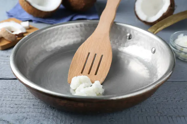 Frying pan with coconut cooking oil and spatula on grey wooden table, closeup
