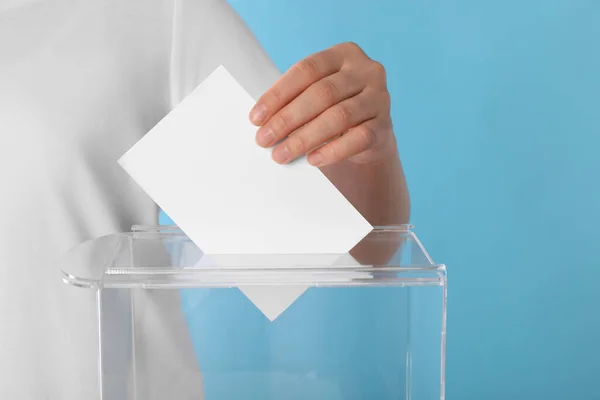 女性把选票放在浅蓝色背景的投票箱里 — 图库照片