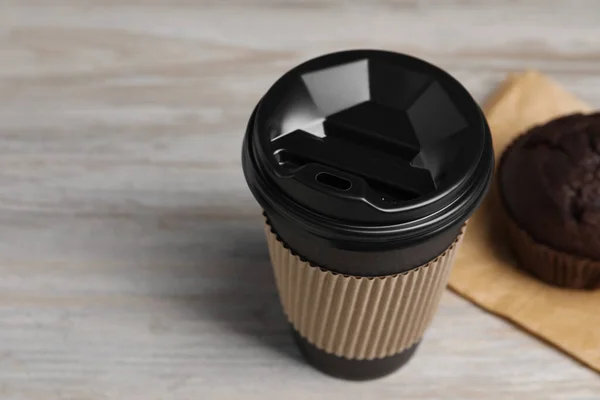 Paper cup with black lid on wooden table, closeup and space for text. Coffee to go