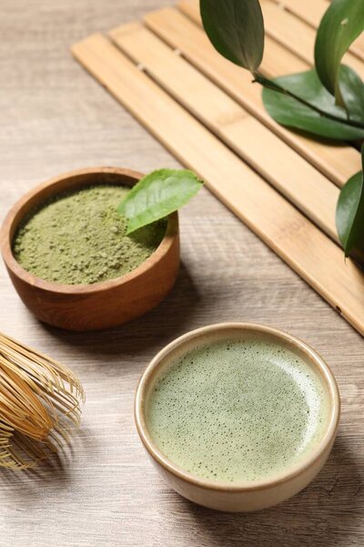 Cup of fresh matcha tea and green powder on wooden table