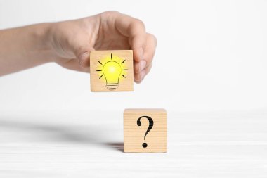 Fikir konsepti. Beyaz ahşap masa üzerinde soru işareti olan bir kadına ampul çizimi ile küp koyan kadın, yakın plan.