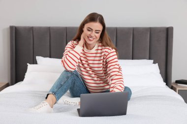 Yatak odasında dizüstü bilgisayarı olan mutlu kadın.