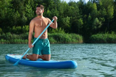 Nehirdeki SUP tahtasına kürek çeken adam.