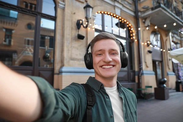 Smiling man in headphones taking selfie outdoors