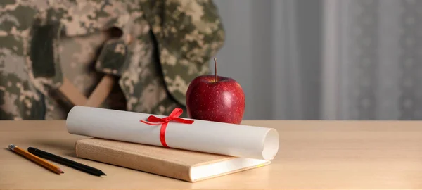 Military education. Diploma, apple and stationery on wooden table, space for text. Chair with soldier\'s jacket indoors