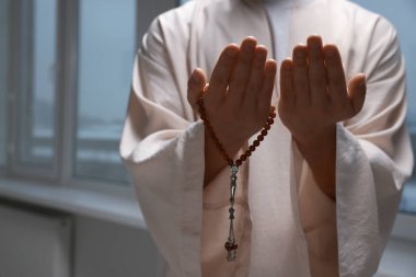 Misbaha 'lı Müslüman bir adam pencerenin yanında dua ediyor, yakın plan. Metin için boşluk