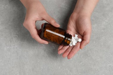 Kadın açık gri masada şişeden eline hap döküyor.