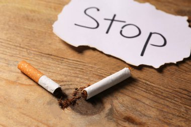 Kırık sigara ve kelime. Tahta masaya yazılı dur, yakın plan. Sigara içilmiyor