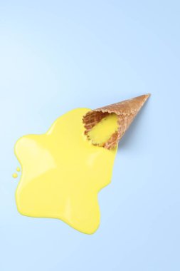 Açık mavi zemin üzerinde erimiş dondurma ve gofret konisi, üst görünüm