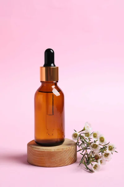 Bottle with cosmetic oil and flowers on pink background