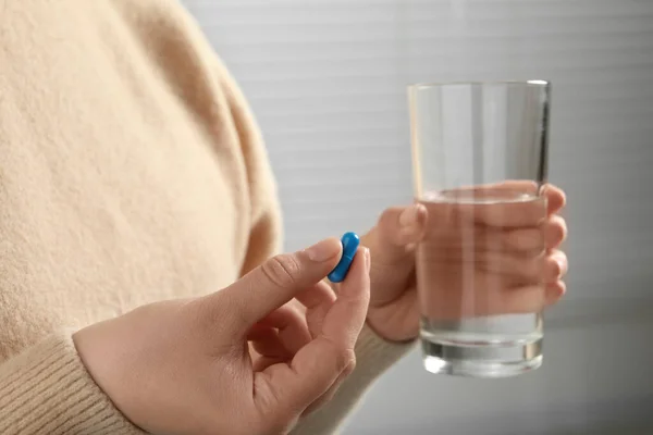 Woman with glass of water and pill on light background, closeup