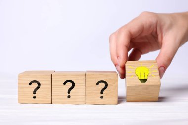 Fikir konsepti. Beyaz ahşap masa üzerinde soru işaretleri olan ampullerin resimleriyle küp koyan kadın, yakın plan.