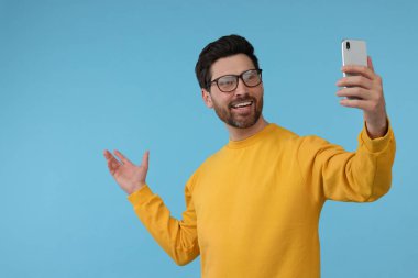 Gülümseyen adam açık mavi arka planda akıllı telefonlu selfie çekiyor, mesaj için boşluk