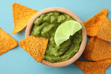 Bir kase lezzetli guacamole, limon ve cips açık mavi ahşap masa, düz uzanmış