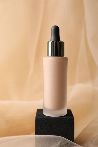 Bottle of skin foundation on beige tulle fabric. Makeup product