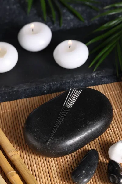 Stones with acupuncture needles and burning candles on bamboo mat