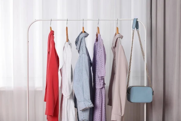 Clothing rack with stylish women's clothes on wooden hangers indoors