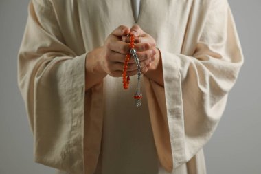 Misbaha 'lı Müslüman adam açık gri arka planda dua ediyor, yakın plan