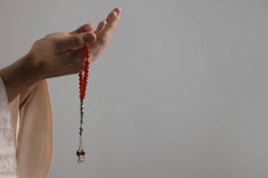 Misbaha 'lı Müslüman bir adam açık gri arka planda dua ediyor, yakın plan. Metin için boşluk