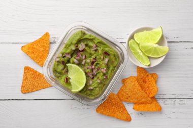 Beyaz ahşap masada soğanlı, limonlu ve cipsli bir kase lezzetli guacamole.