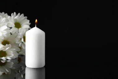 Yanan mum ve siyah ayna yüzeyinde beyaz kasımpatı çiçekleri karanlıkta, yazı için boşluk. Cenaze sembolleri