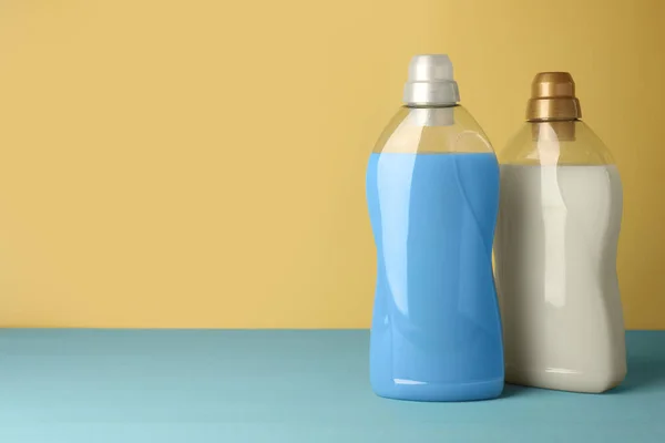 Bottles of fabric softener on light blue table, space for text