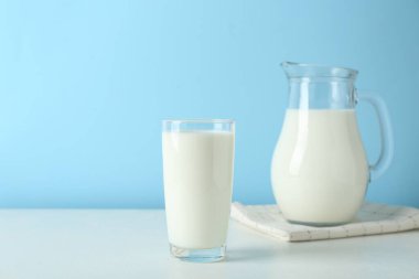 Sürahi ve bir bardak taze süt açık mavi arka planda beyaz masada.