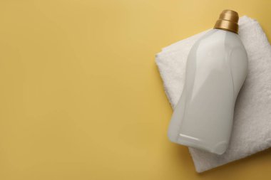 Soluk sarı arka planda bir şişe yumuşatıcı ve Terry Havlu, üst manzara. Metin için boşluk