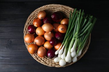 Siyah ahşap masada farklı soğan çeşitleri olan hasır hasırlar, üst manzara.
