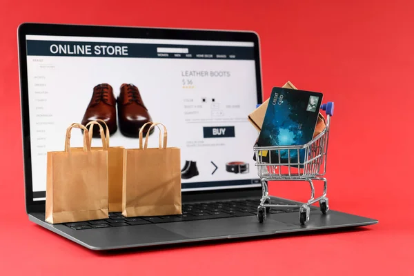 Online store. Laptop, small shopping cart, purchases and credit card on red background