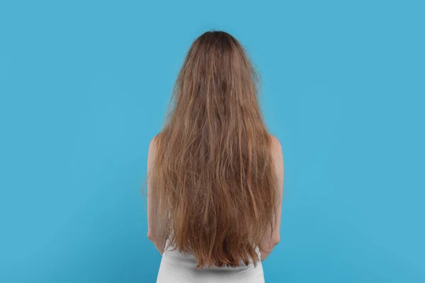 Woman with damaged hair on light blue background, back view