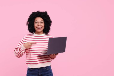 Pembe arka planda dizüstü bilgisayar gösteren mutlu genç bir kadın. Metin için boşluk