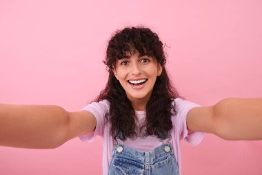 Güzel bir kadın pembe arka planda selfie çekiyor.