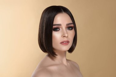 Bej arka planda kahverengi saçlı güzel bir genç kadının portresi.