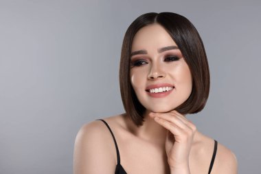 Gri arka planda gülümseyen kahverengi saçlı güzel bir genç kadının portresi.