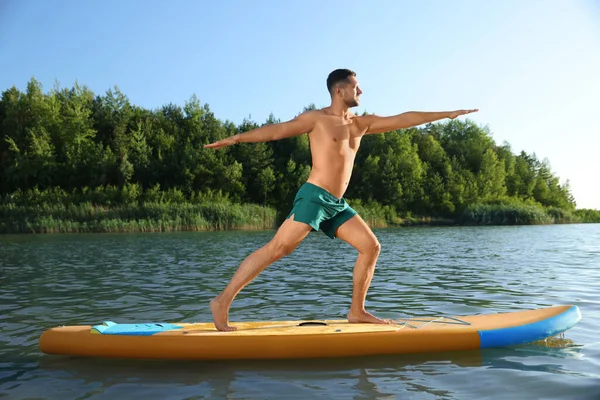 男人在河边的彩色Sup板上练习瑜伽 — 图库照片