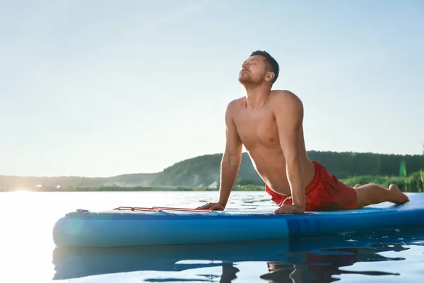 日落时分 男人在河边浅蓝色的Sup板上练习瑜伽 — 图库照片