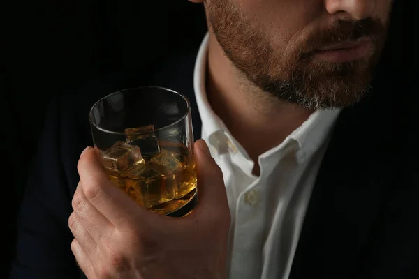 Man holding glass of whiskey with ice cubes on black background, closeup