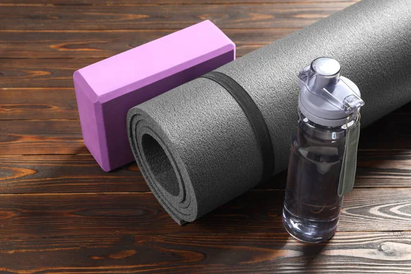 Exercise mat, yoga block and bottle of water on wooden floor