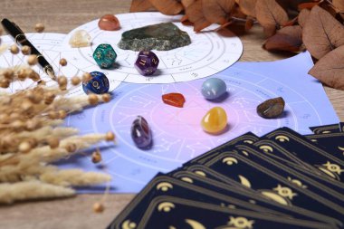 Zodyak çarkı, tarot kartları, astroloji zarları ve ahşap masa üzerindeki değerli taşlar, yakın plan.