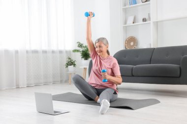 Üst düzey kadın evde internet üzerinden ders izlerken dambıllarla egzersiz yapıyor. Spor malzemeleri.