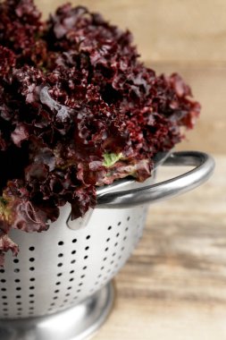 Ahşap masada kırmızı mercan marullu Colander, yakın plan.