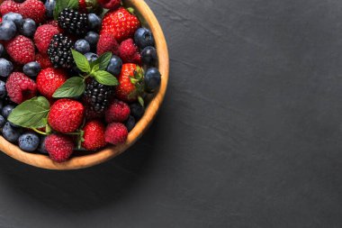 Siyah masadaki ahşap kasede bir sürü taze olgun böğürtlen. Metin için boşluk